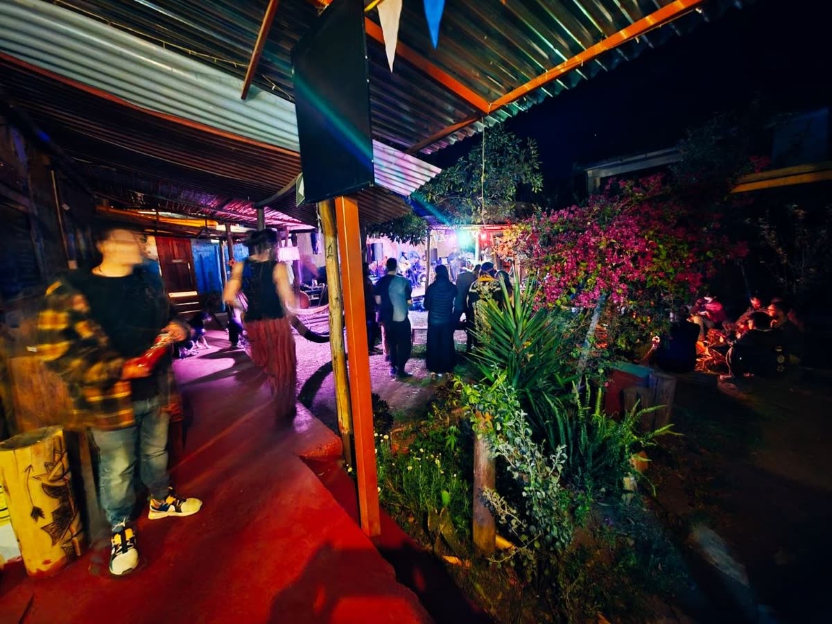 el patio del hostal de noche: bajo el techo pasa la gente, al fondo el público junto al es